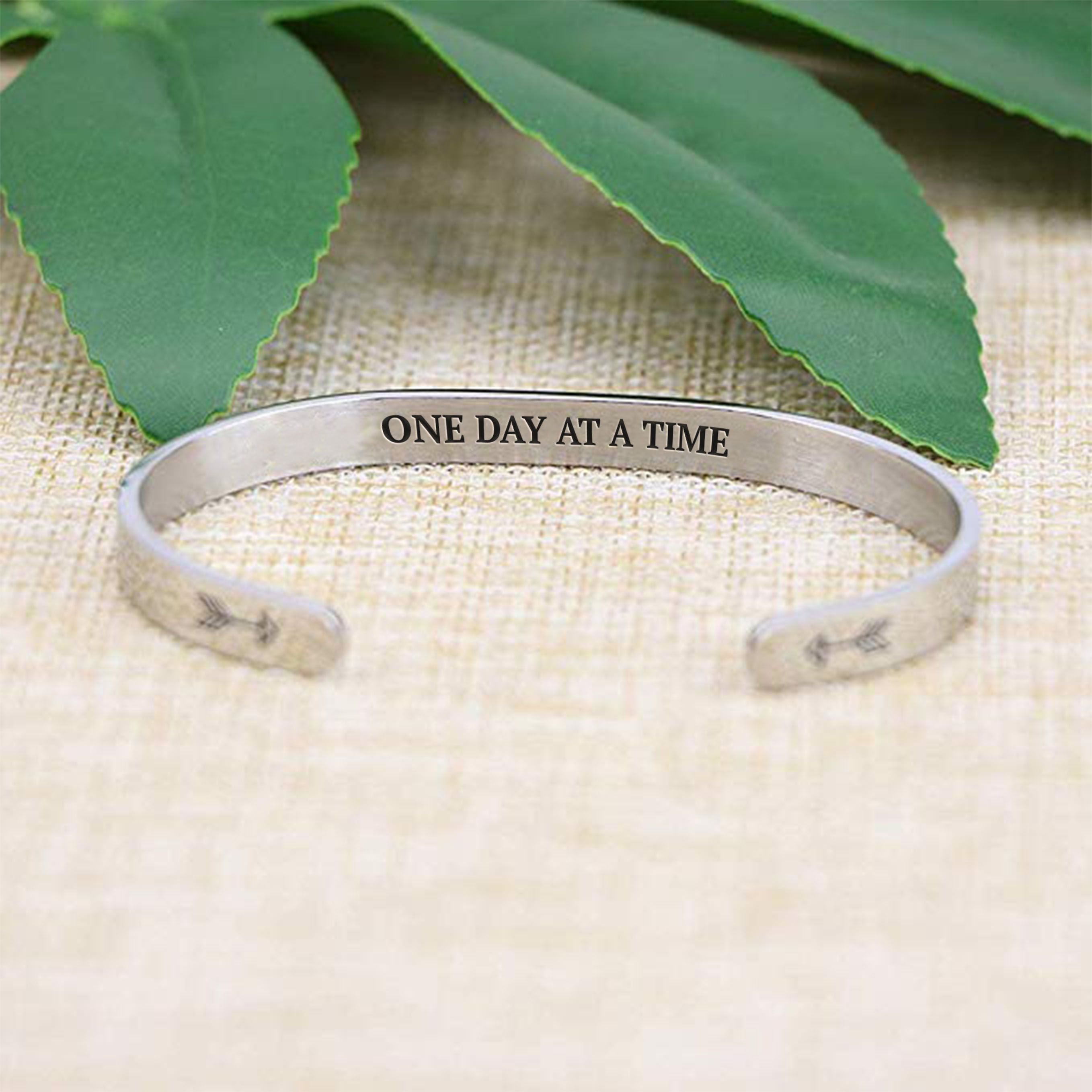 One day at a time bracelet with silver plating with message in focus on a burlap surface with a leafy background
